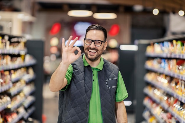 A salesman is standing at the marketplace and showing okay gesture at the camera