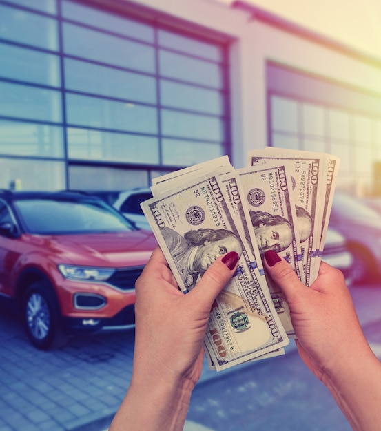 Salesman selling auto in car shop or businessman buying new car holding dollar in hand