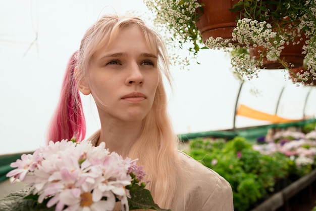 Salesperson of garden mall holding blossoming plant in pot in hands standing in greenhouse