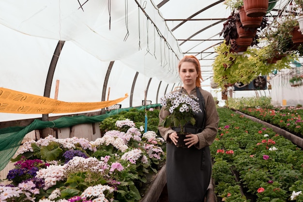 Salesperson shows blossoming plant in pot standing in greenhouse of gerden mall