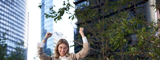 Photo saleswoman expresses joy and happiness businesswoman triumphing on street raising hands up