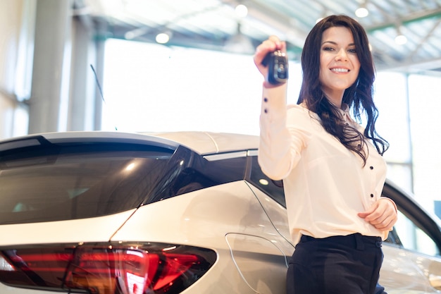 Saleswoman with key present a new car in dealership center