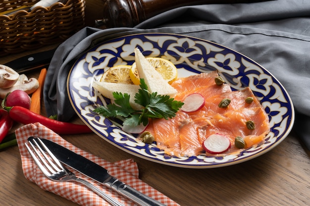 Salmon carpaccio with capers, radish and lemon on a plate with a traditional Uzbek 