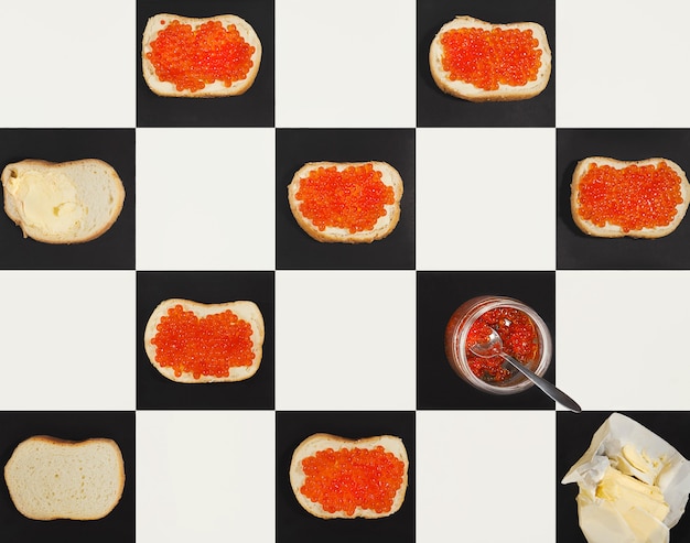 Photo salmon caviar canapes, butter, red caviar in a jar forming a pattern on chess bords