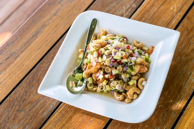 Salmon fillet crispy spicy salad Thai style in white plate with spoon on the wooden table