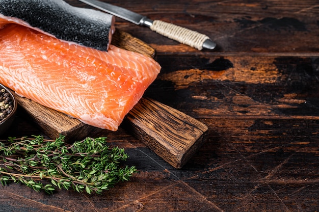 Filetto di salmone su una tavola di legno con erbe e sale. fondo in legno scuro. vista dall'alto. copia spazio.