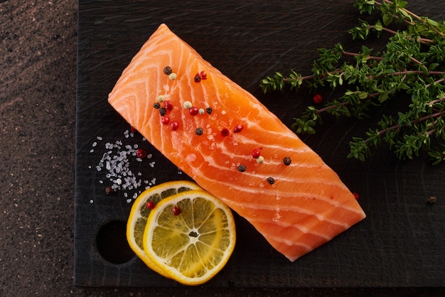 Salmon fillet steak and seasoning on dark wooden cutting board on brown table