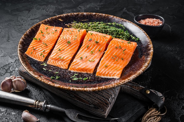 Salmon fillet steaks, raw fish with thyme and herbs. Black background. Top view.