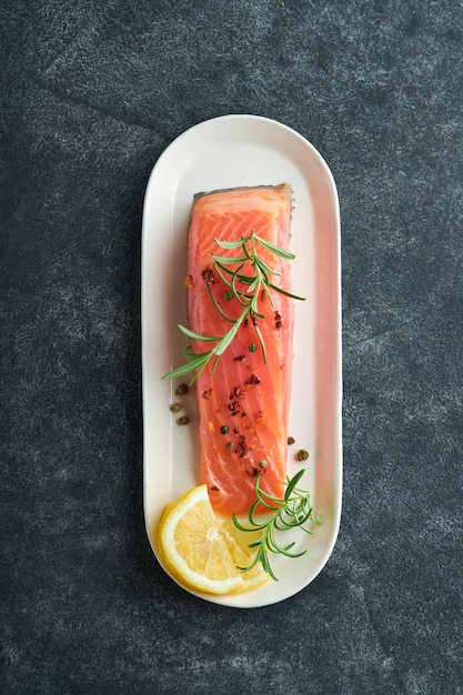 Salmon fish piece Fresh raw salmon fish piece on marble board stand with herbs and lemon on black background Seafood or menu concept Top view