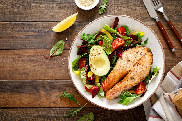 Salmon fish steak grilled avocado and fresh vegetable salad with tomato bell pepper and leafy vegetables Top view