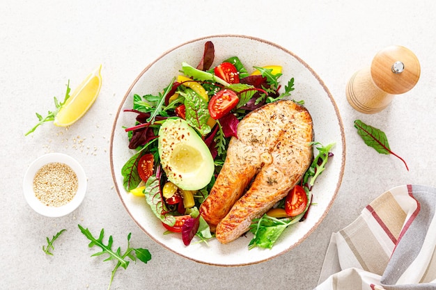 Salmon fish steak grilled avocado and fresh vegetable salad with tomato bell pepper and leafy vegetables Top view