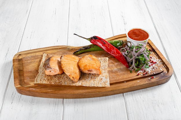 Salmon kebabs with grilled vegetables and red sauce on wooden desk