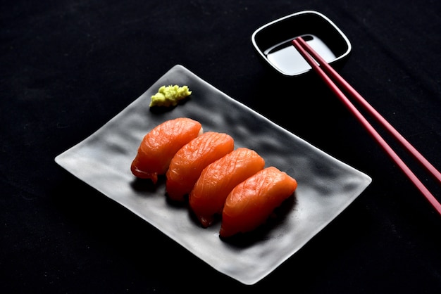 Photo salmon nigiri sushi and wasabi sauce with chopsticks on black valvet.