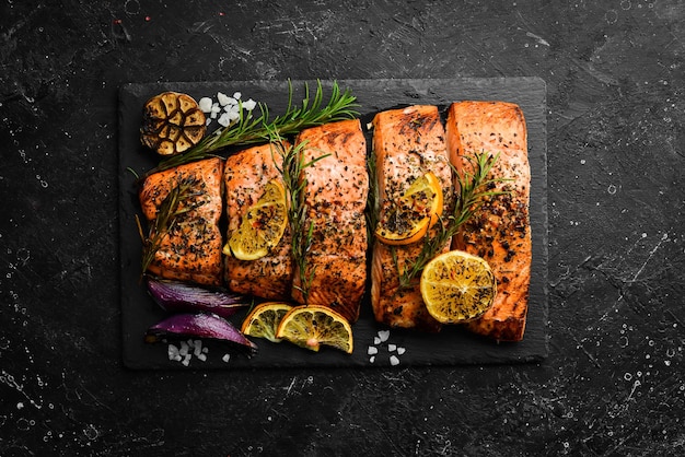 Salmon. Pieces of grilled fish on a black stone background. Recipe. Seafood. Free space for text.