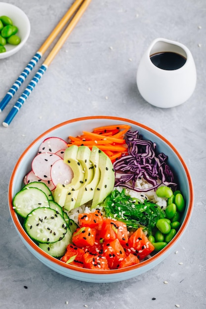 Salmon poke bowl with rice avocado seaweed pickled carrots cucumber radishes and edamame beans