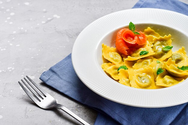 Salmon ravioli traditional Italian food with fresh basil in a white plate on a grey stone table. Recipe Italian food. food flat lay