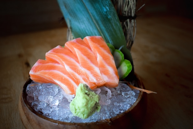 Salmon raw sashimi on brown Japanese traditional dish on black table. Closed up.