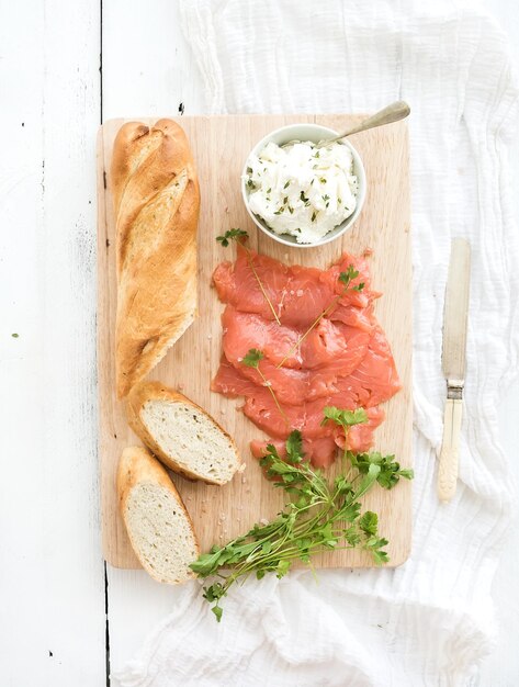 Salmon ricotta and fresh parsley with baguette on a rustic wooden board over white wood background Top view