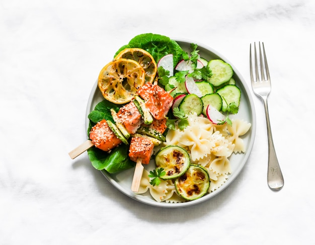 Spiedini di salmone arrosto con pasta di zucchine e insalata di verdure su sfondo chiaro vista dall'alto delizioso pranzo sano ed equilibrato