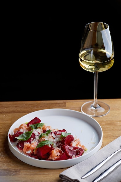 Foto insalata di salmone con formaggio di barbabietola e foglie verdi su un tavolo di legno con un bicchiere di vino bianco.