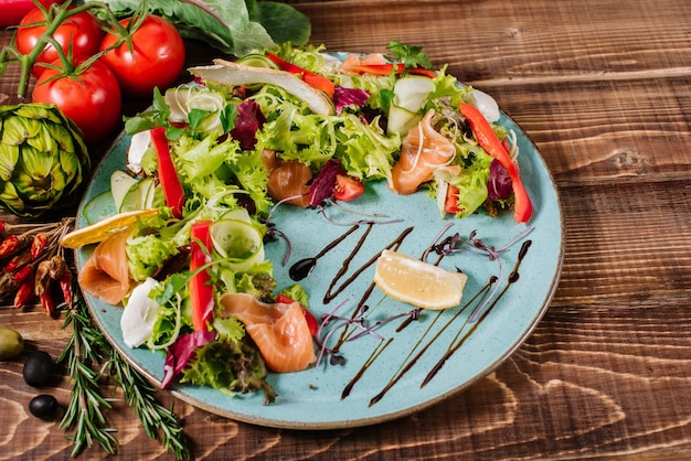 Salmon salad with vegetables and herbs on wooden background