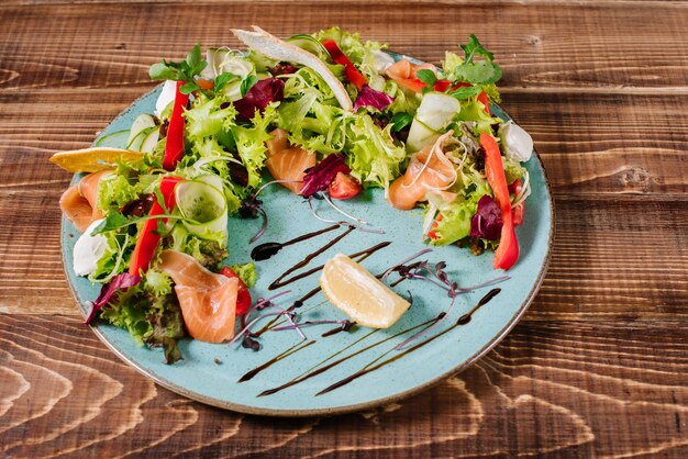Salmon salad with vegetables and herbs on wooden background