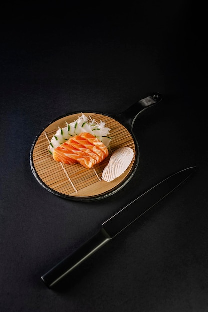 Salmon sashimi with a black knife on a black background