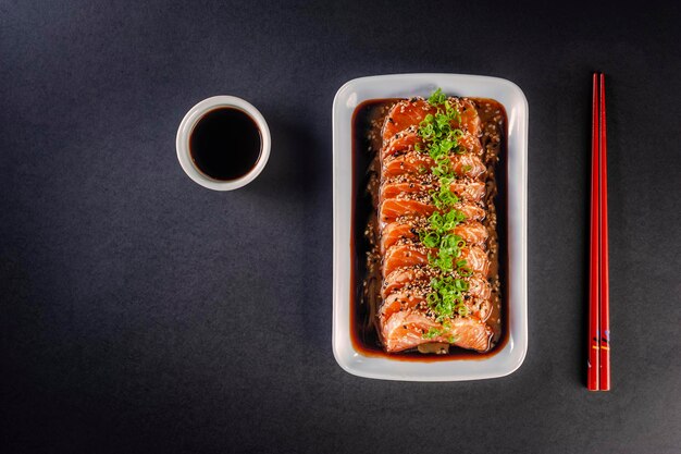 Salmon sashimi with sesame, shoyu and miso sauce on a black table. Top view.