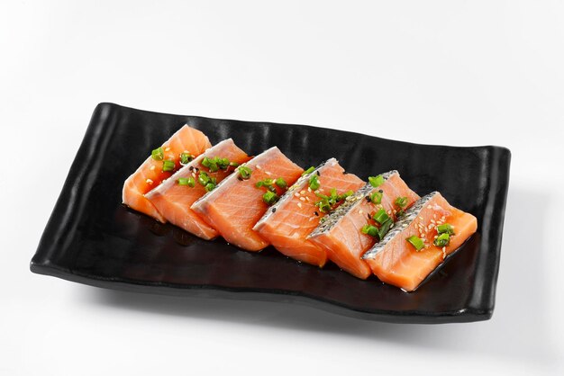 Salmon Sliced Top arranged in a black plate green vegetables sprinkled on top