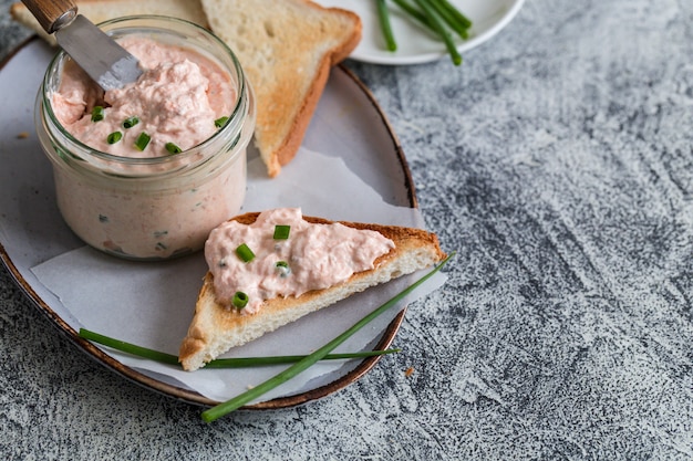 연어와 부드러운 크림 치즈가 항아리에 퍼졌습니다. 연어 rillettes, 무스, 페이트 및 회색 배경에 토스트