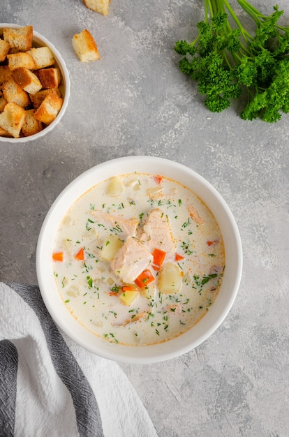 Foto zuppa di salmone con panna, patate, carote, erbe e crostini in una ciotola su fondo di cemento