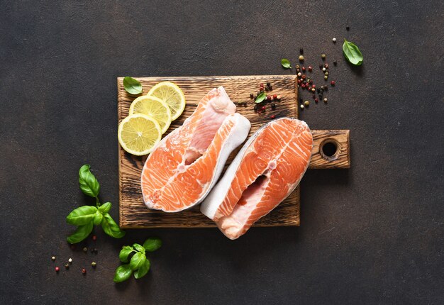 Salmon steak raw fish with spices prepared for cooking on a wooden board on a dark concrete background.