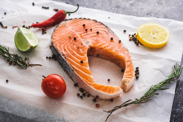 サーモンステーキ、赤い魚は羊皮紙の上にあり、レモンペッパートマトとハーブの隣にあります