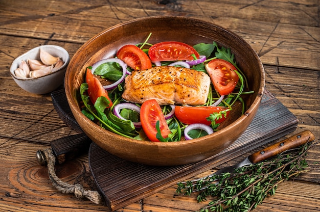 나무 접시에 녹색 잎 Arugula, 아보카도, 토마토와 연어 스테이크 샐러드. 나무 배경입니다. 평면도.