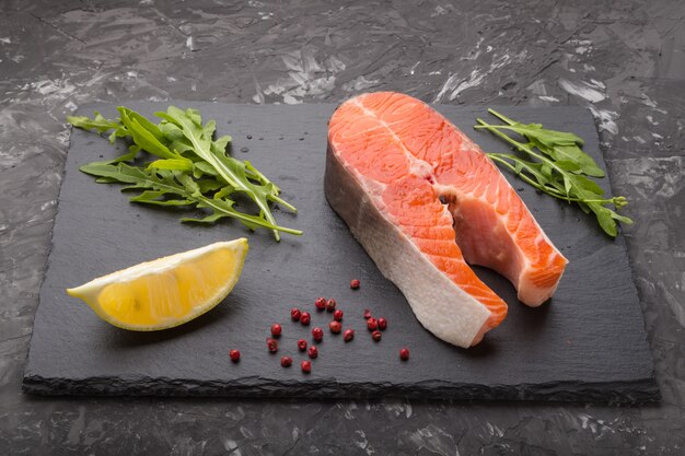 Salmon steak with arugula and lemon on a black slate board. Side view.