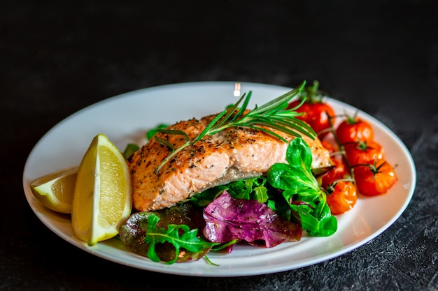 Photo salmon steak with lettuce, cherry tomatoes and lemon slices. gala dinner. food for lunch. grilled red fish. baked salmon in the oven