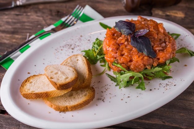 Salmon tartare with arugula and croutons rustic table