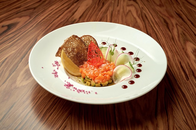 Salmon tartare with avocado and sauce in a white plate on a wooden background