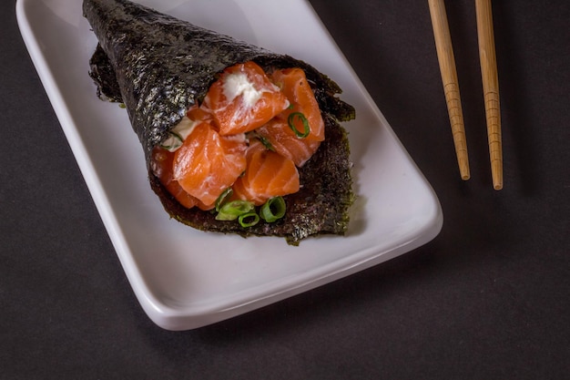 Salmon temaki sushi on white plate in black background.