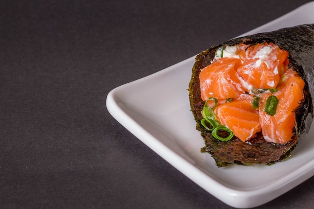 Foto sushi di temaki di color salmone sul piatto bianco nella superficie nera