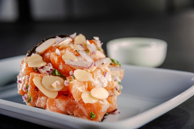 Salmon temaki with almond blades and purple onion on white plate in black background.