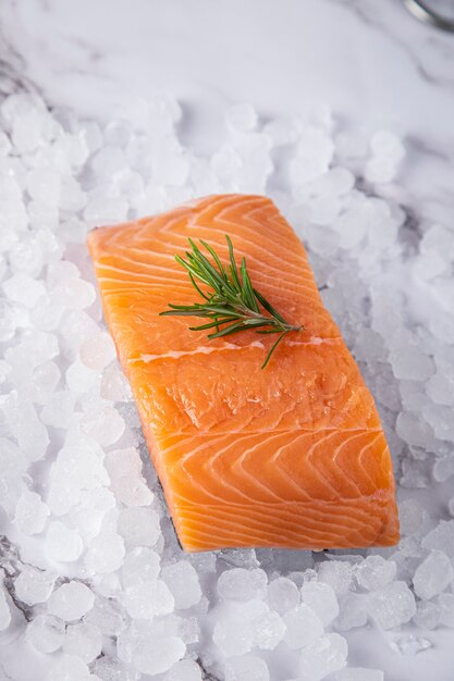 Photo salmon with a sprig of rosemary on ice on a white marble surface