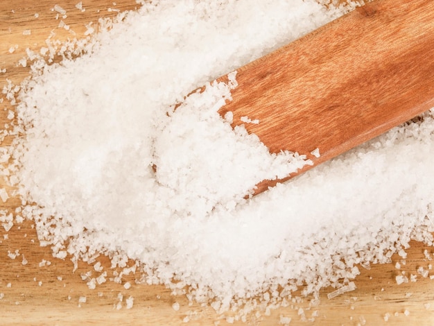 Salt in flakes on a wooden spoon and on a wooden table