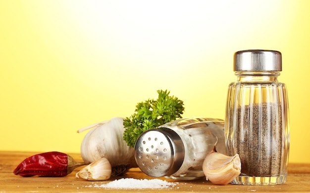 Salt and pepper mills garlic and parsley on wooden table on yellow background