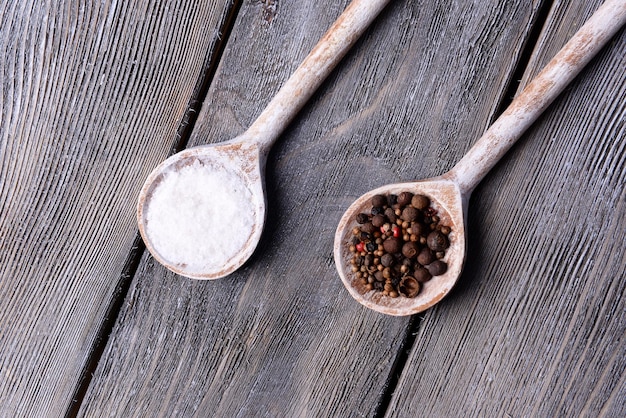 Photo salt and pepper in spoon on wooden table closeup