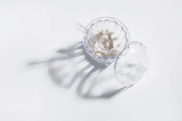 Salt or sugar in transparent jar with shadow on white