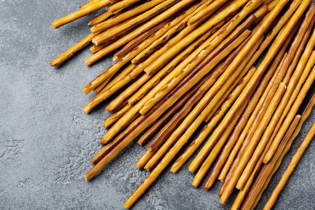 Salted bread sticks or long crunchy salty pretzel sticks on parchment paper on old gray stone or concrete table. Top view.