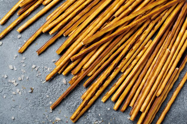 Salted bread sticks or long crunchy salty pretzel sticks on parchment paper on old gray stone or concrete table. Top view.