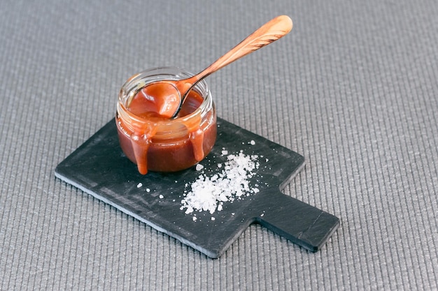 Salted caramel in a jar on a gray background on a stone stand. Side view.