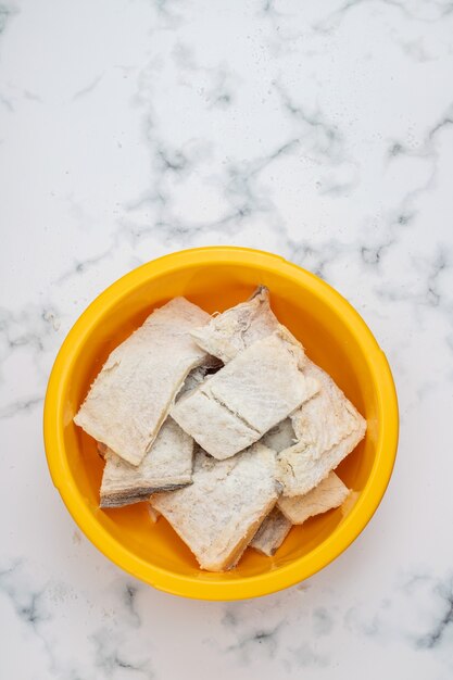 Salted dry cod fish in big yellow plastic bowl